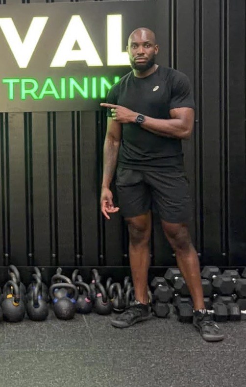 Train With Prime coach standing in the gym with kettlebells and dumbbells